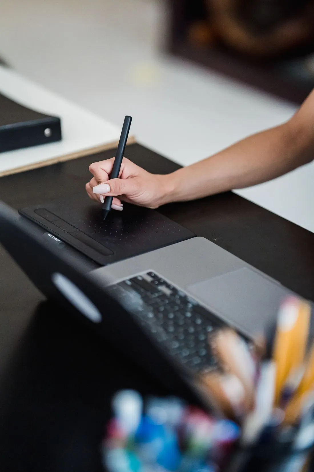 A hand draws on a graphics tablet next to a laptop.