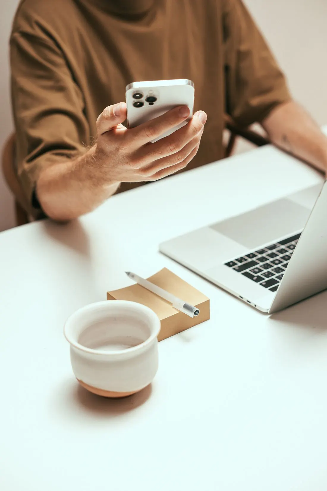 A person checks their phone in front of their laptop.